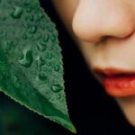 Detailed shot of a dewy leaf next to a person's face, highlighting nature's freshness and human connection.