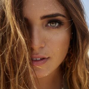 Intimate close-up portrait of a woman with beach sand in her hair, conveying a natural and serene vibe.